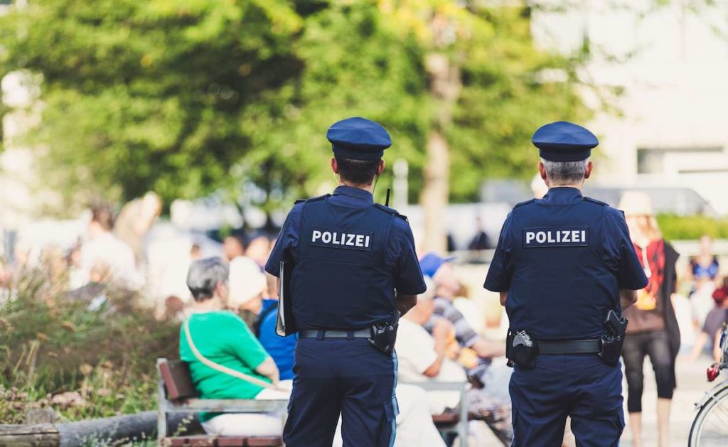 Two German cops have their back turned to the camera. Their shirts read "polizei"
