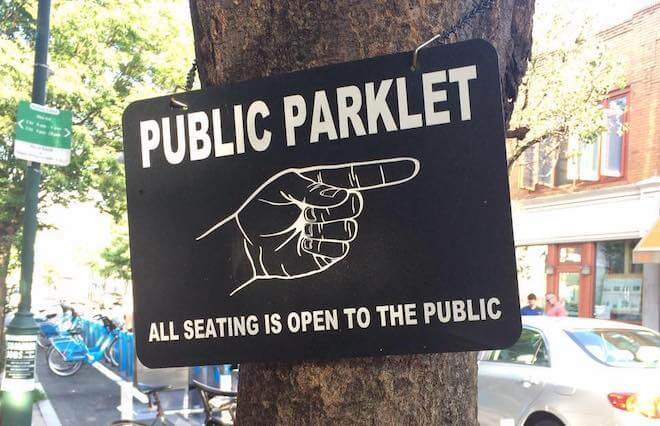 A black sign with white lettering reads "PUBLIC PARKLET" with a hand pointing to the right.