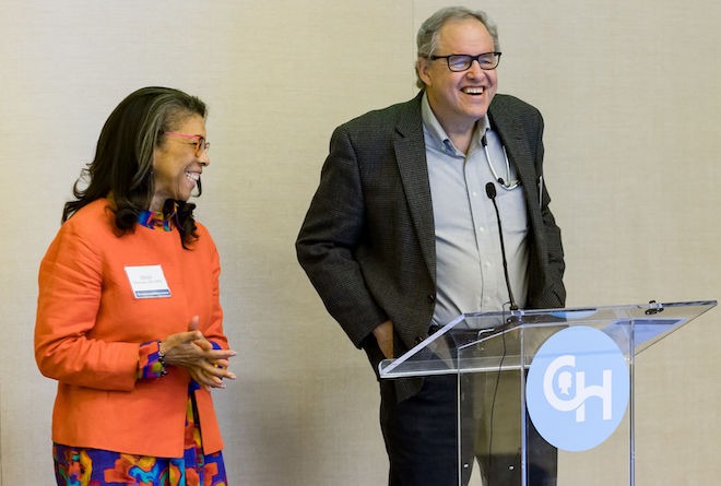 Doctors Alexis A. Thompson (left) and Stephan A. Grupp of the Children's Hospital of Philadelphia stand side by side during a presentation. Thompson, an African American woman with long, straight hair, wears glasses, a nametag, an orange jacket over a multicolored dress, stands beside Grupp, a White man with thinning hair, glasses, an unbuttoned suit jacket, button-down shirt and slacks, standing behind a clear podium with the Children's Hospital of Philadelphia logo, a large C and H.